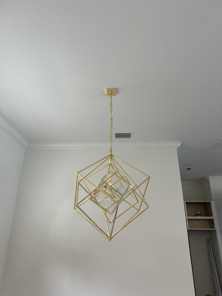 Gold nested-cube chandelier hung from a white dining-room ceiling with crown molding