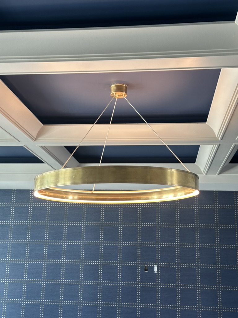 Large brass ring chandelier hung from a coffered ceiling with navy inset panels