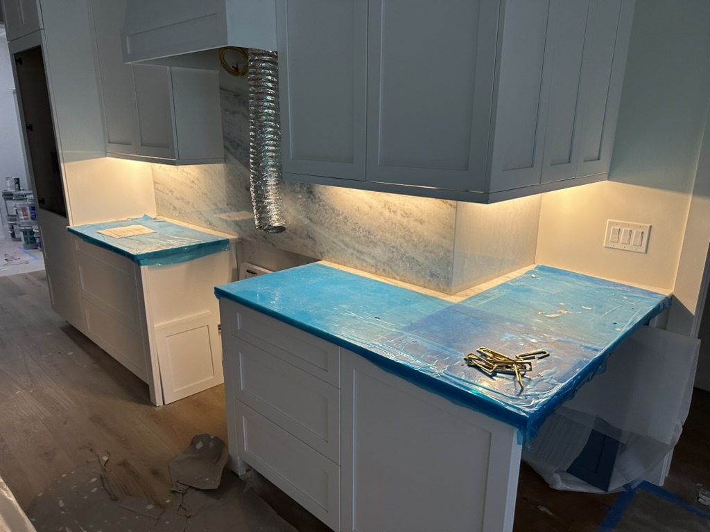 Warm undercabinet LED lighting along a kitchen with white cabinets and stone backsplash during remodel