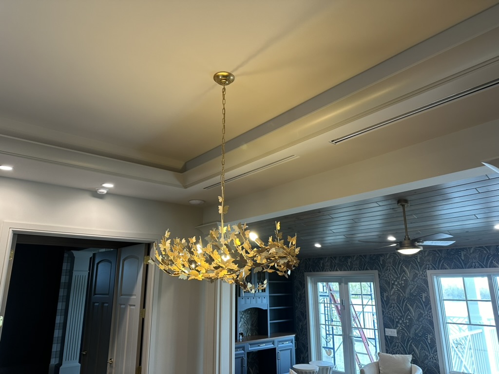 Gold botanical leaf chandelier on a chain in an open living space with coffered ceiling