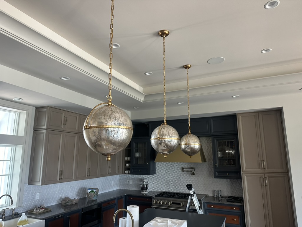 Mercury-glass globe pendants over the kitchen island with navy and taupe cabinets and a gold range hood