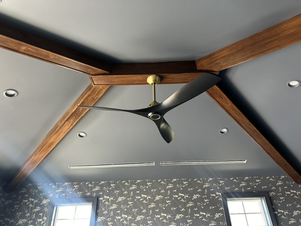 Three-blade ceiling fan with brass canopy in a vaulted ceiling framed by wood beams