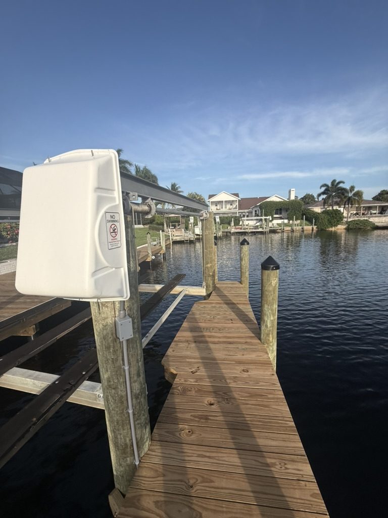 Boat lift motor cover with a No Swimming sign and conduit running down the piling to the dock