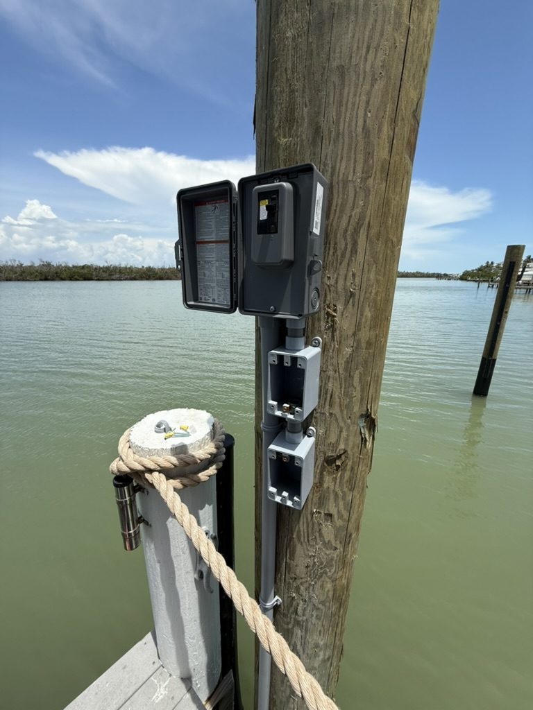 Dock piling with the Square D disconnect door open and two empty device boxes below it, before the receptacles were installed