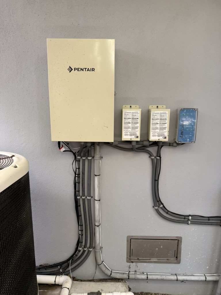 Pentair pool equipment panel with two pool light transformers and the pool water leveler, conduit runs below