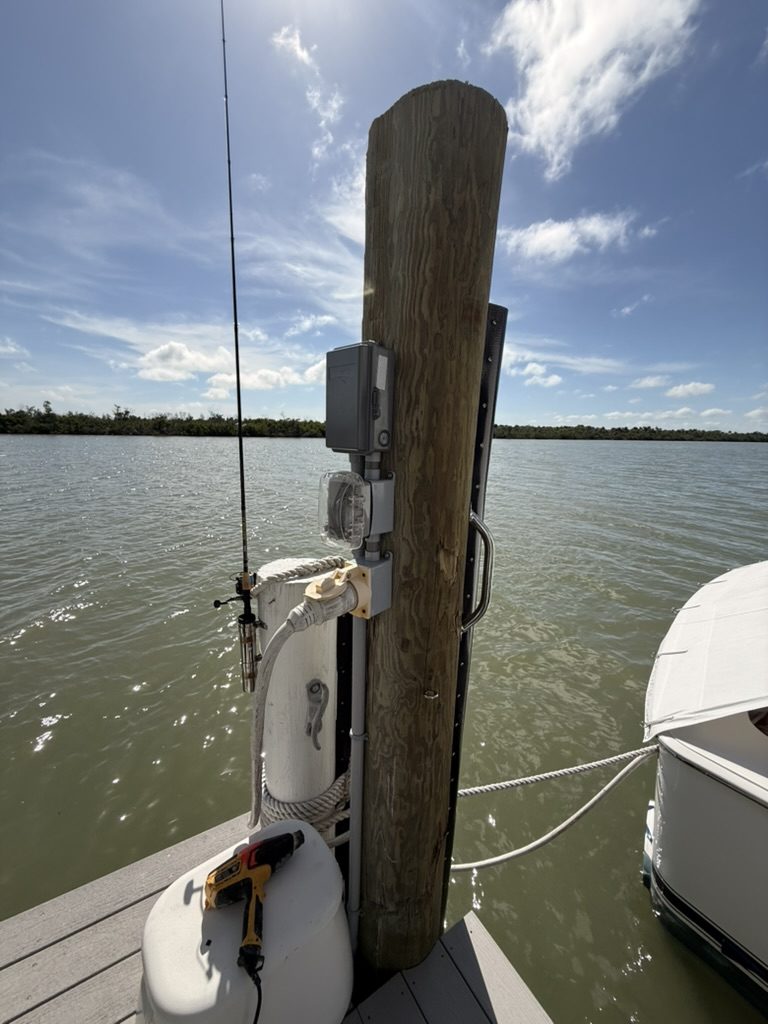 Finished dock piling with a Square D disconnect, a 120-volt receptacle under a clear cover and the shore power receptacle with a boat cord plugged in