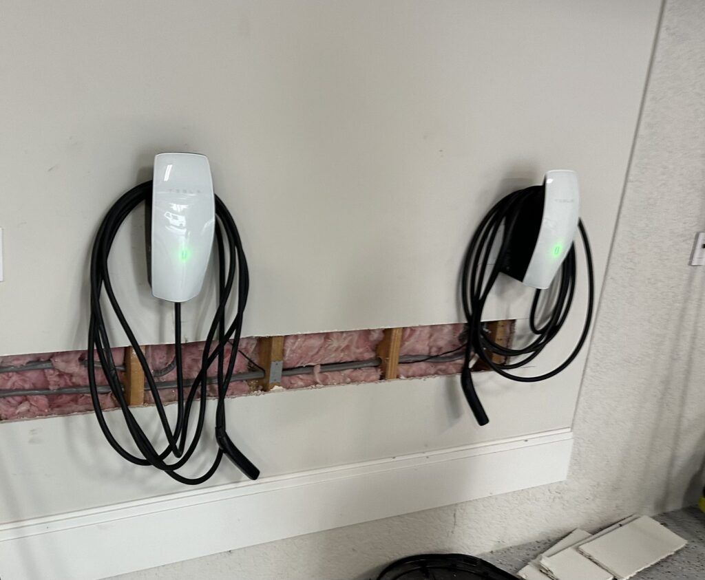 Two Tesla chargers installed side by side, with the drywall opening used to run the wiring, before patching