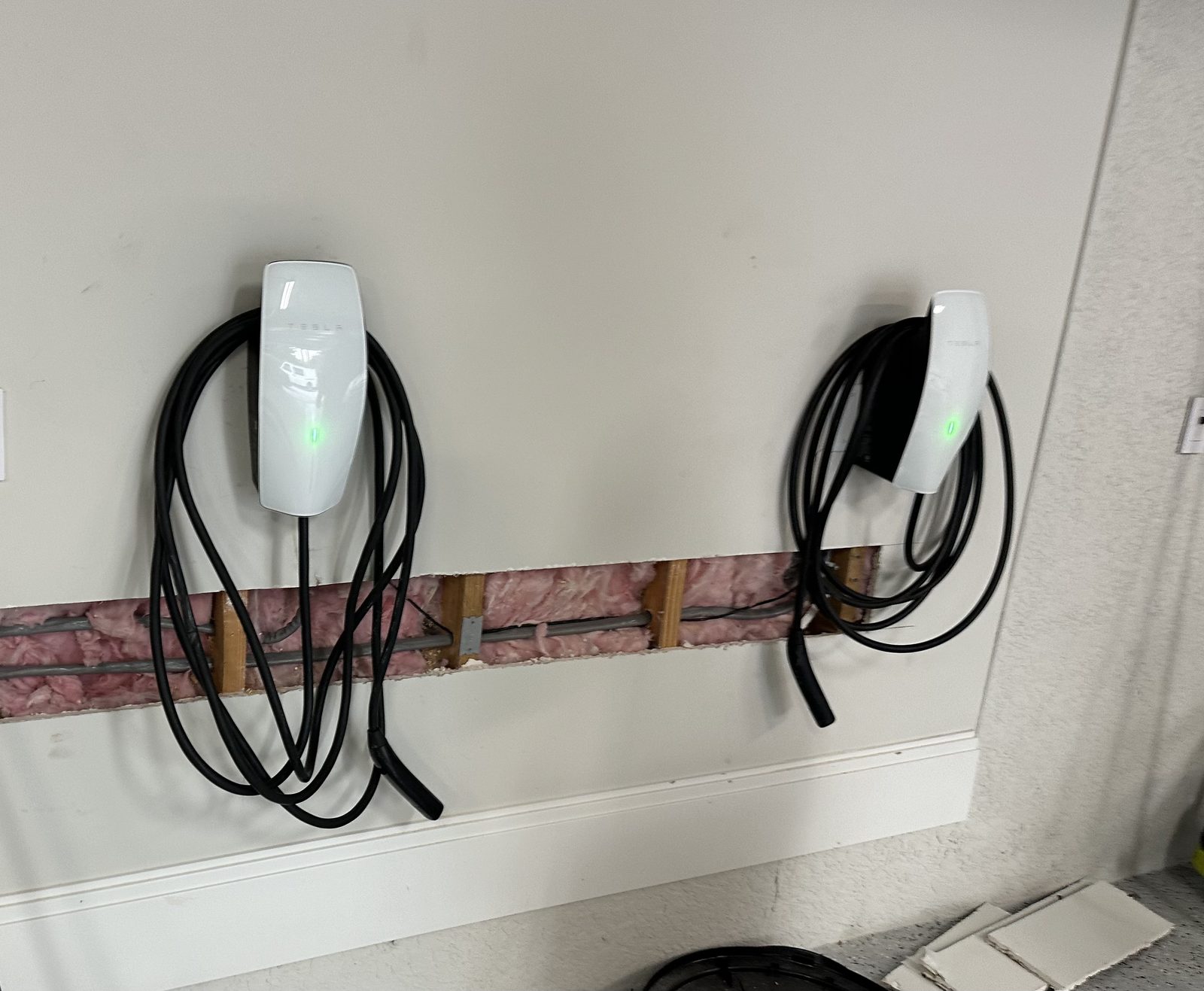 Two Tesla chargers installed side by side, with the drywall opening used to run the wiring, before patching
