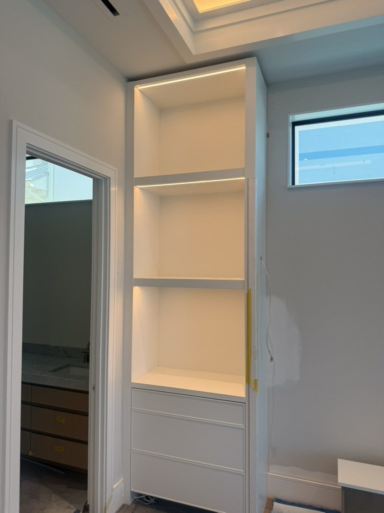 White built-in shelving with LED tape under the shelves, beside a lit ceiling cove